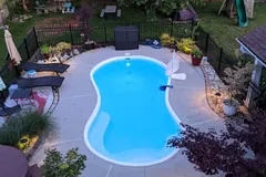Finished backyard pool surrounded by paving, planted borders, seating, and landscape lights
